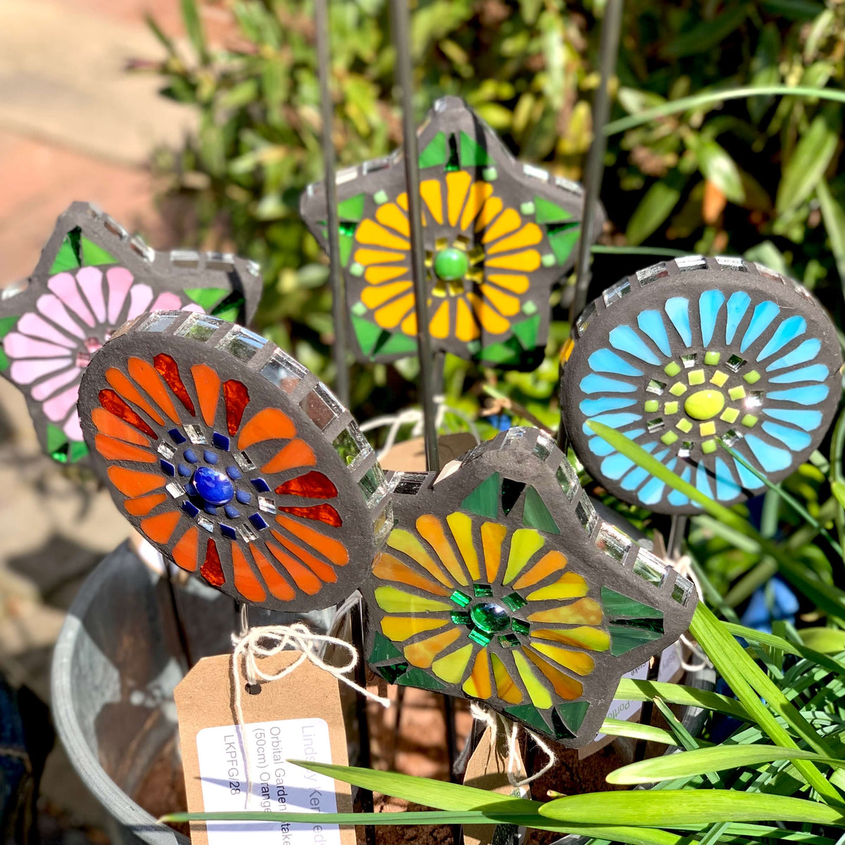 Handmade mosaic flower shaped garden stakes, in orange, yellow, pink and blue.