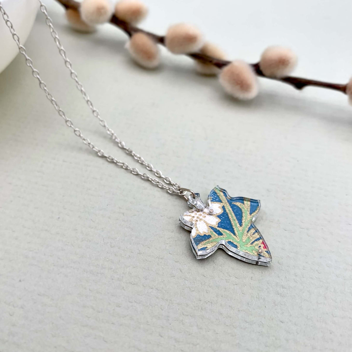 Handmade silver necklace with a colourful leaf pendant, made up of blue and green floral hand painted paper, sandwiched between two pieces of perspex.