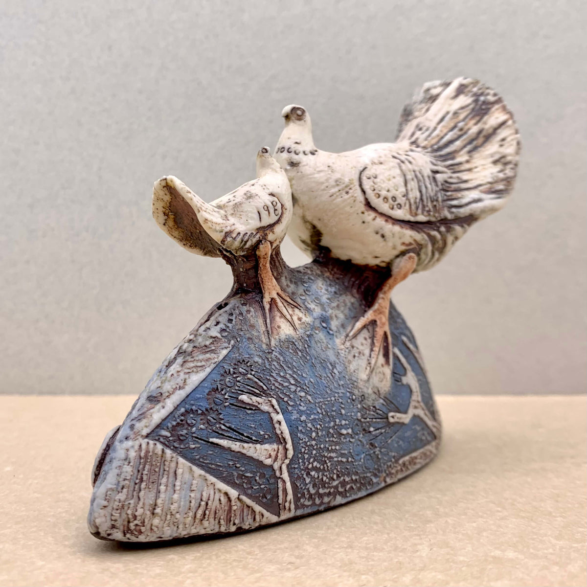 Blandine Anderson handcrafted porcelain sculpture of a smaller dove facing a larger dove. With colour contrasts of teal blue, subtle burgundy and porcelain and a rich texture on the base and dove wings. Available at Ferrers Gallery.