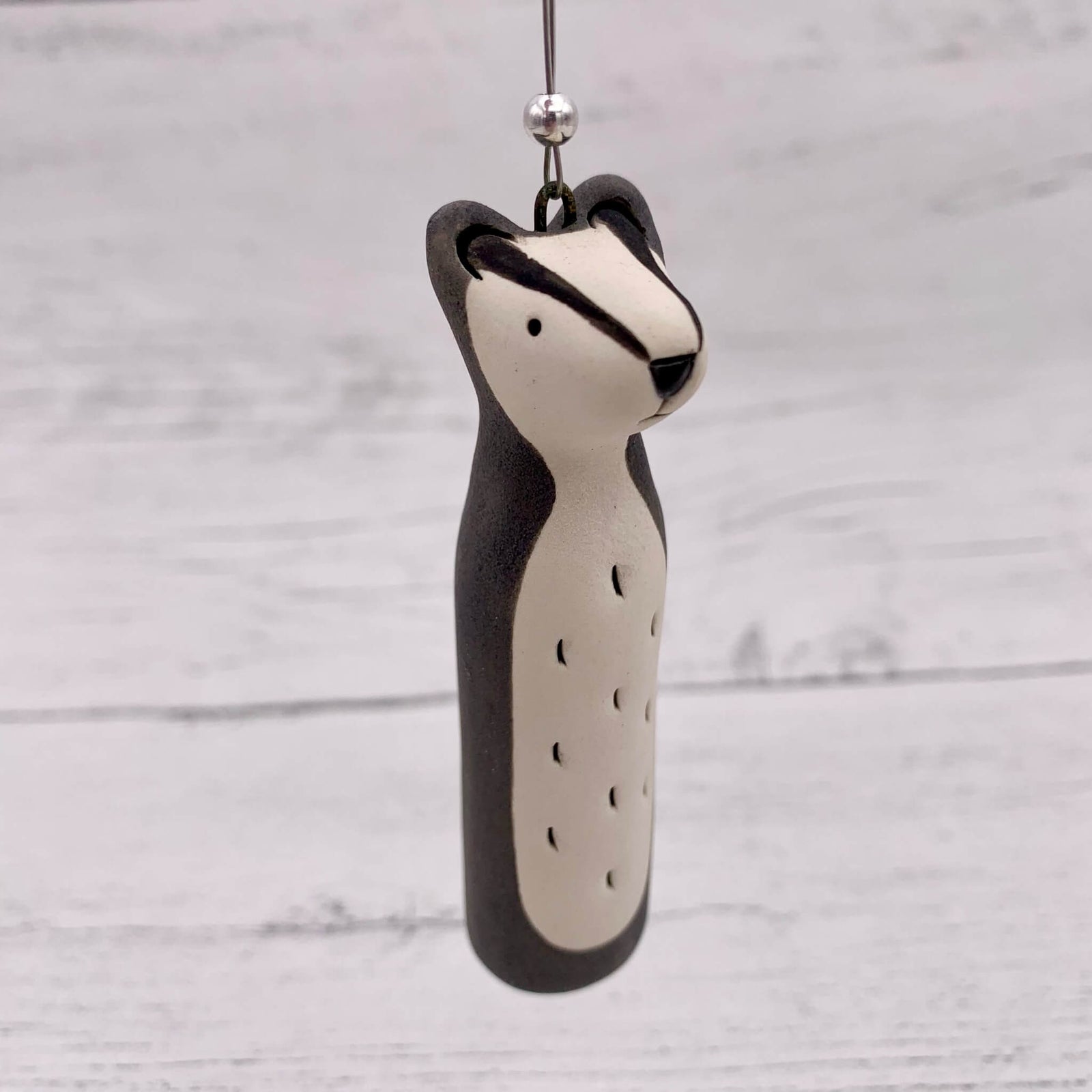 Handmade ceramic hanging decoration, of a badger with a silver bead threaded on.