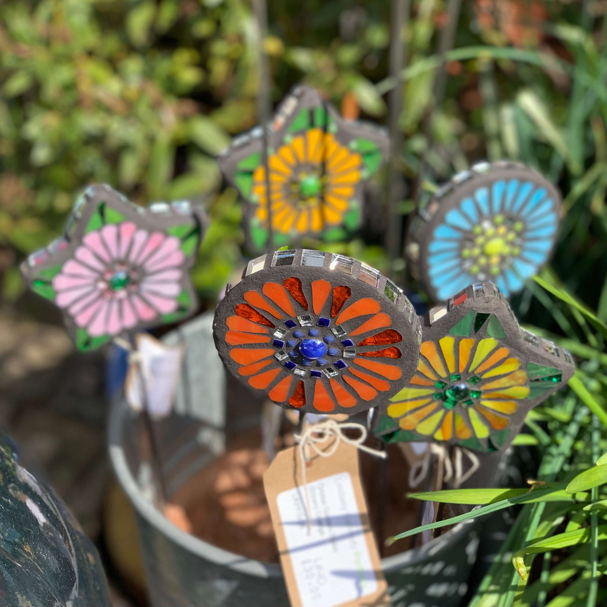 Handmade colourful flower shaped garden stakes, in pink, blue, orange and yellow. 