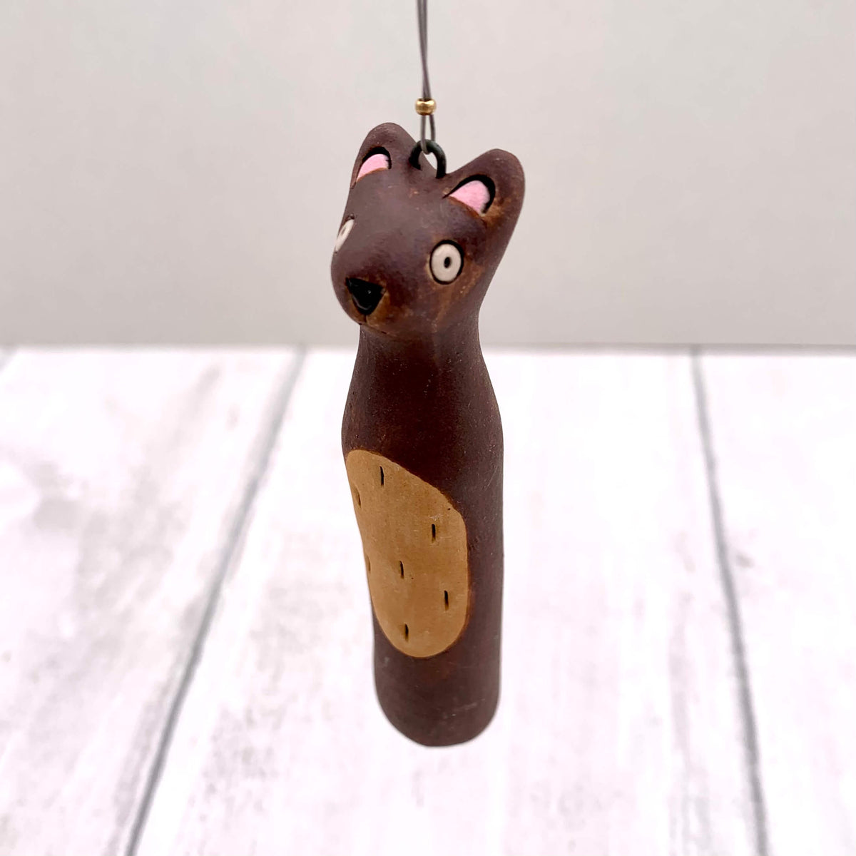 Handmade ceramic hanging of a brown bear, with a tan belly and tiny gold bead.