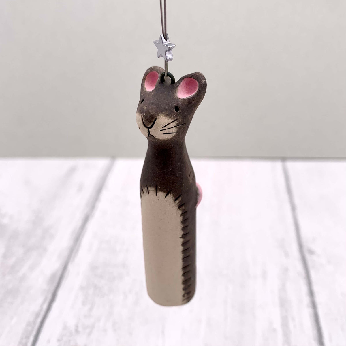 Handmade ceramic hanging of a grey mouse, with a pink tail and silver star.