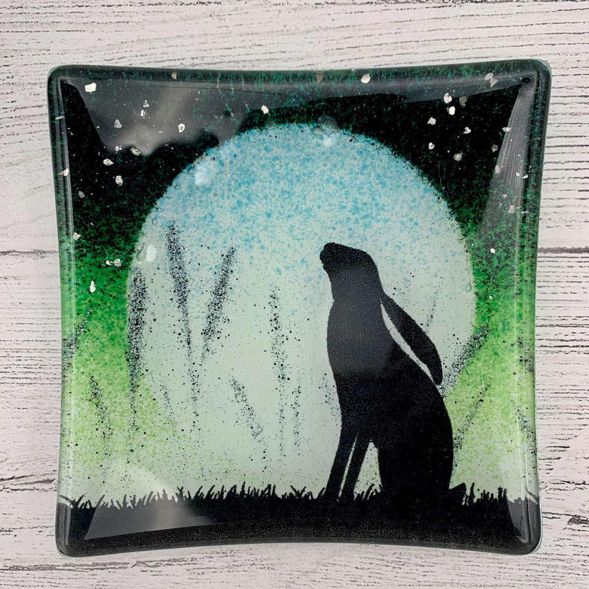Handcrafted in the uk, fused glass jewellery dish in green, with a hare silhouette, large moon and glitter for stars.