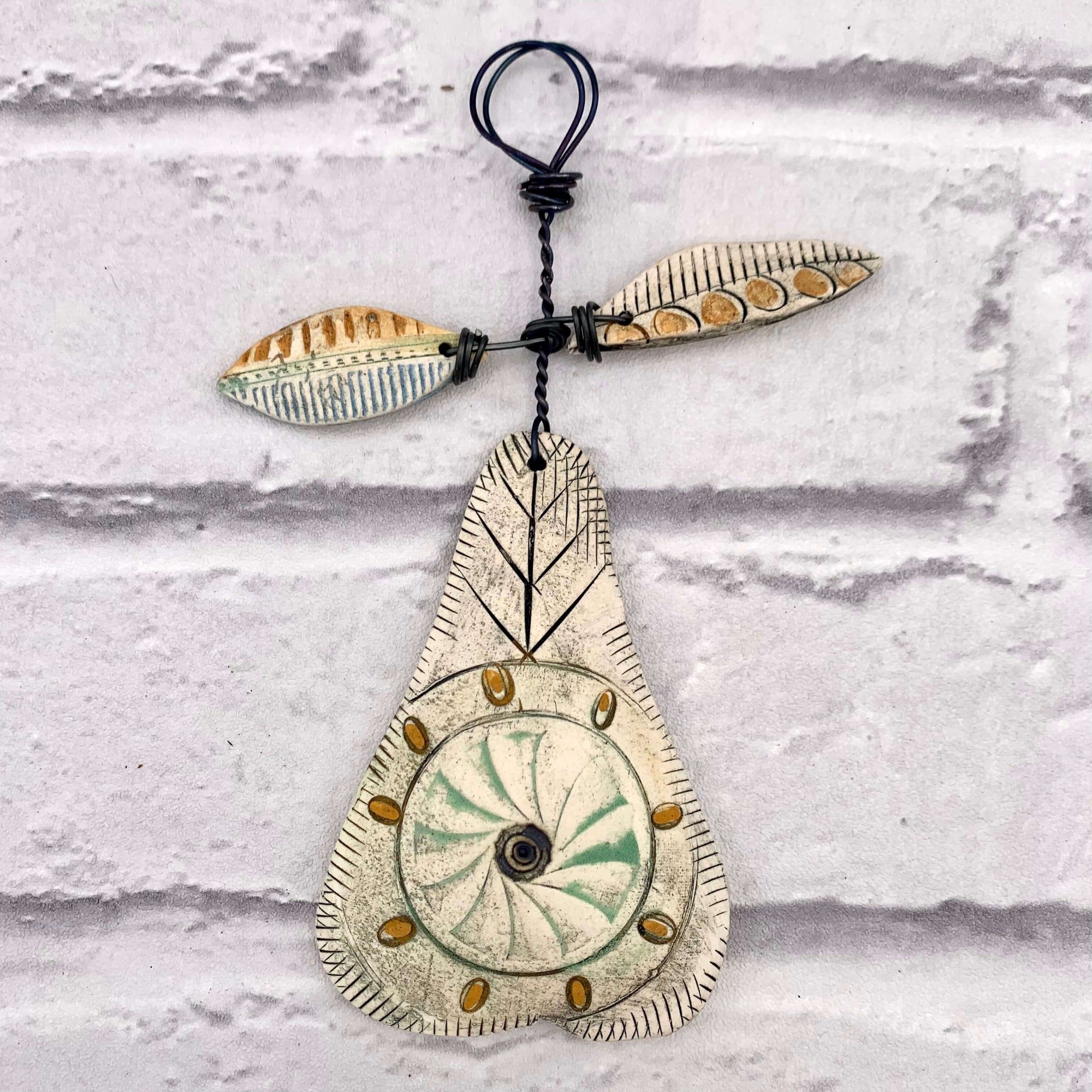 Handmade ceramic pear decoration, with orange and green glazing, hanging from a thick wire with two ceramic leaves. Crafted by Shirley Vauvelle.