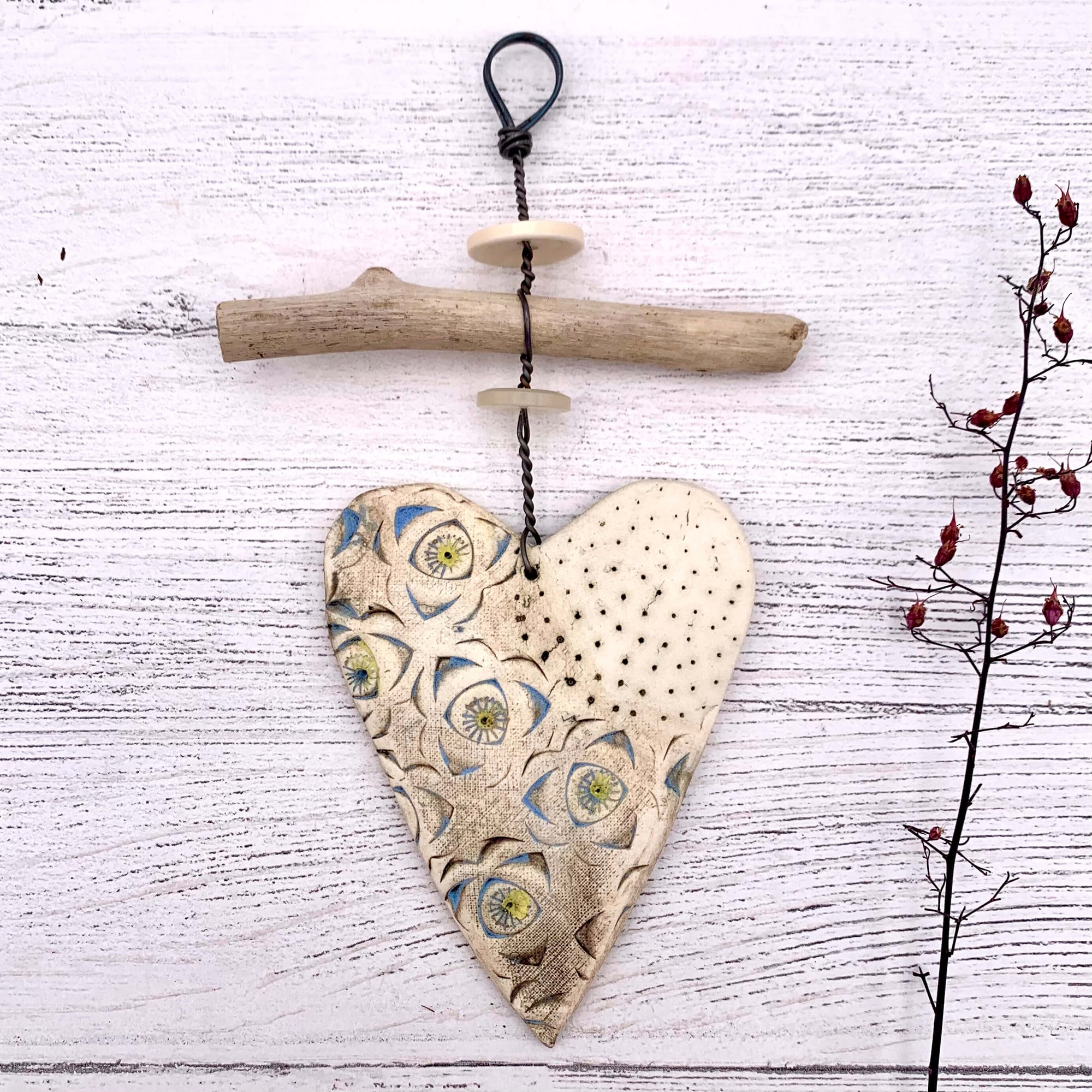 Handmade ceramic heart hanging decoration, by Shirley Vauvelle. This ceramic heart hangs on a thick piece of wire, with driftwood and buttons. 
