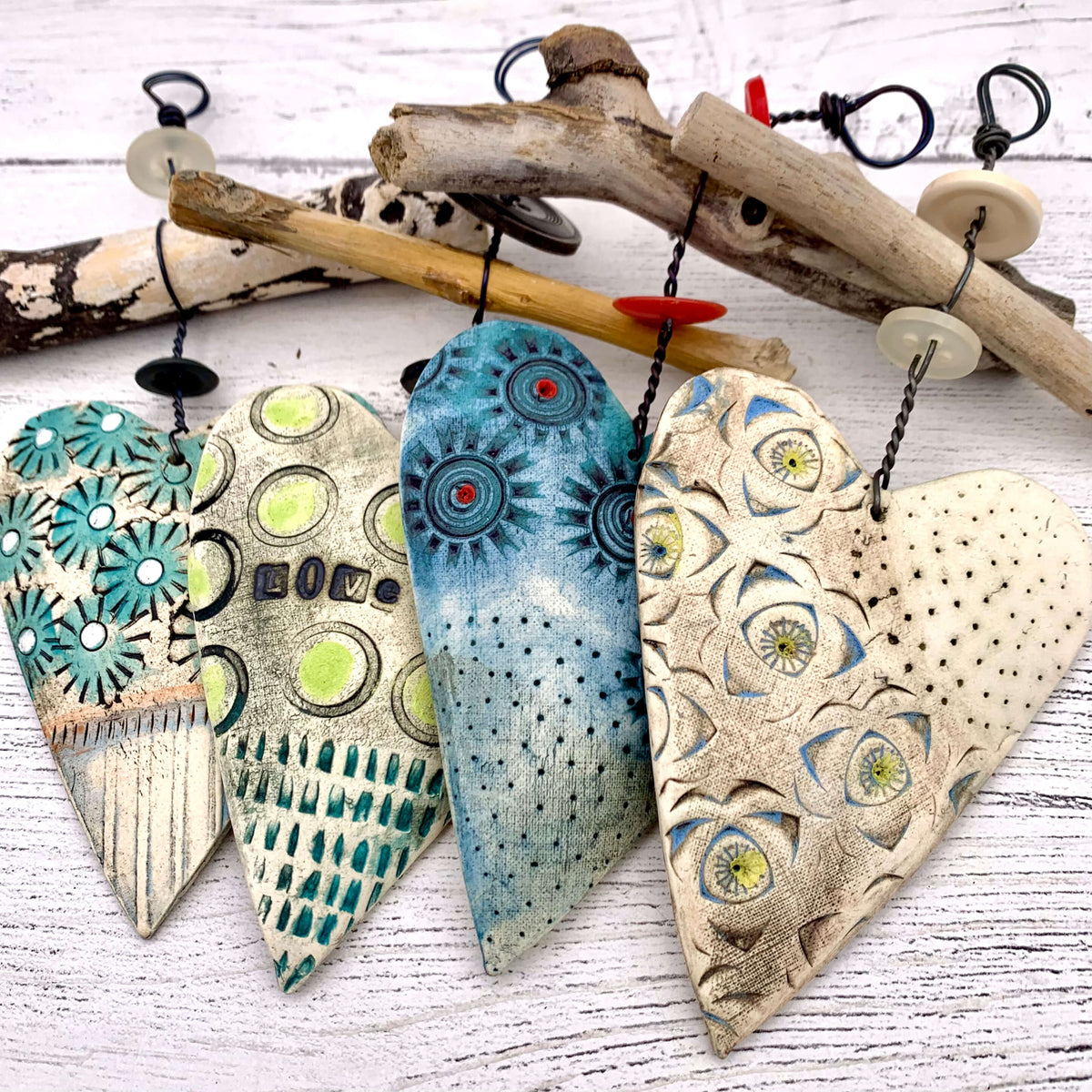 Handmade ceramic heart hanging decorations, by Shirley Vauvelle. These ceramic hearts hang on a thick piece of wire, with driftwood and buttons.