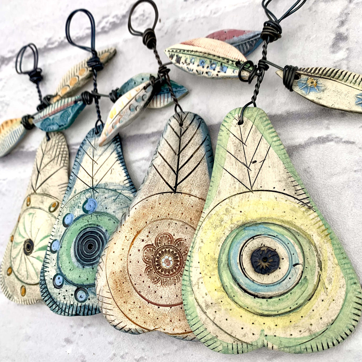 Handmade ceramic pear hanging decorations, with coloured glazing, hanging from a thick wire with two ceramic leaves on each. Crafted by Shirley Vauvelle.